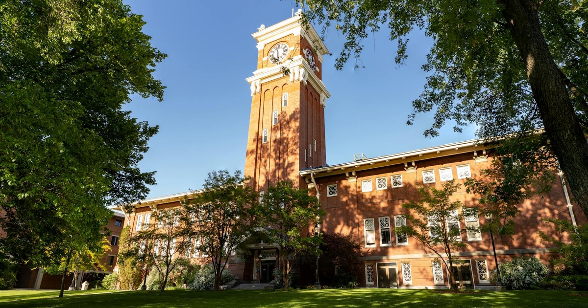 Beautiful view of the iconic clock tower at WSU under a clear blue sky, surrounded by lush greenery.