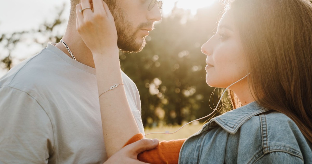 A loving couple shares earphones and a tender moment in a sunny outdoor setting.