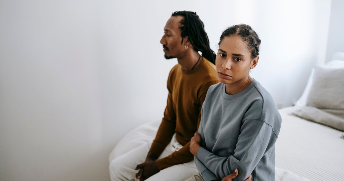 Frustrated thoughtful African American couple in casual wear sitting close on soft bed after quarrel