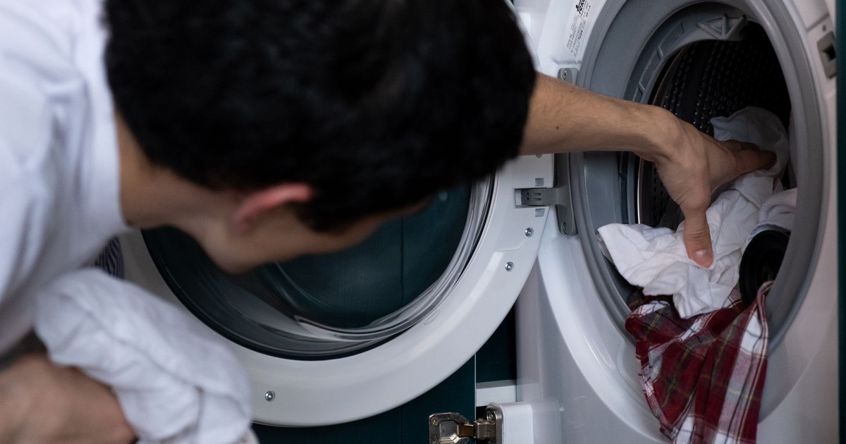 Close-up of a man placing clothes into a washing machine during household chores.