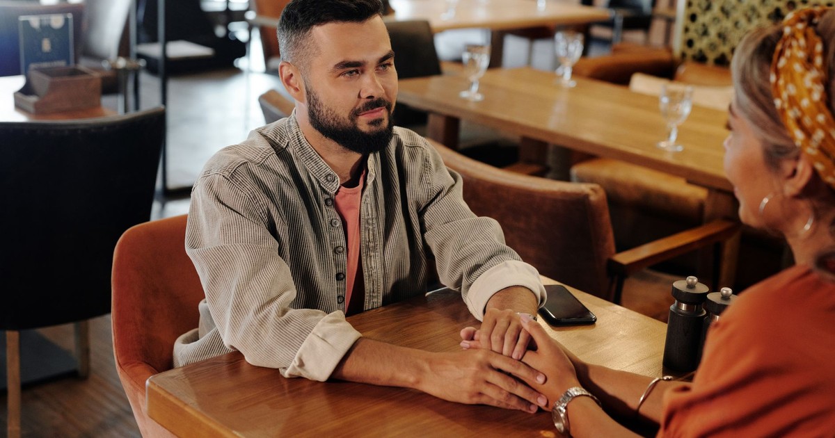 A couple enjoys a romantic moment holding hands at a cozy café, creating a warm atmosphere.