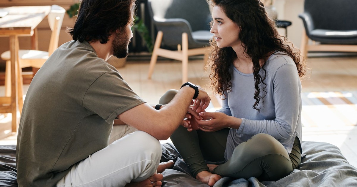 A couple sitting closely on a bed, engaged in a thoughtful discussion in a cozy home setting.
