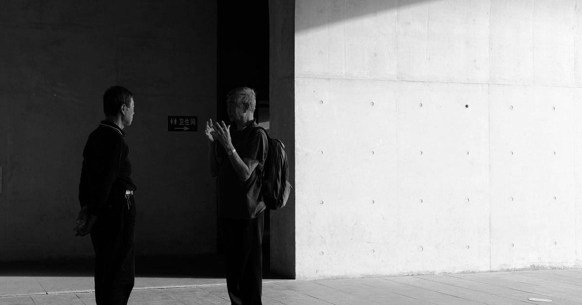 Two men engaged in conversation, silhouetted by light against a concrete wall.