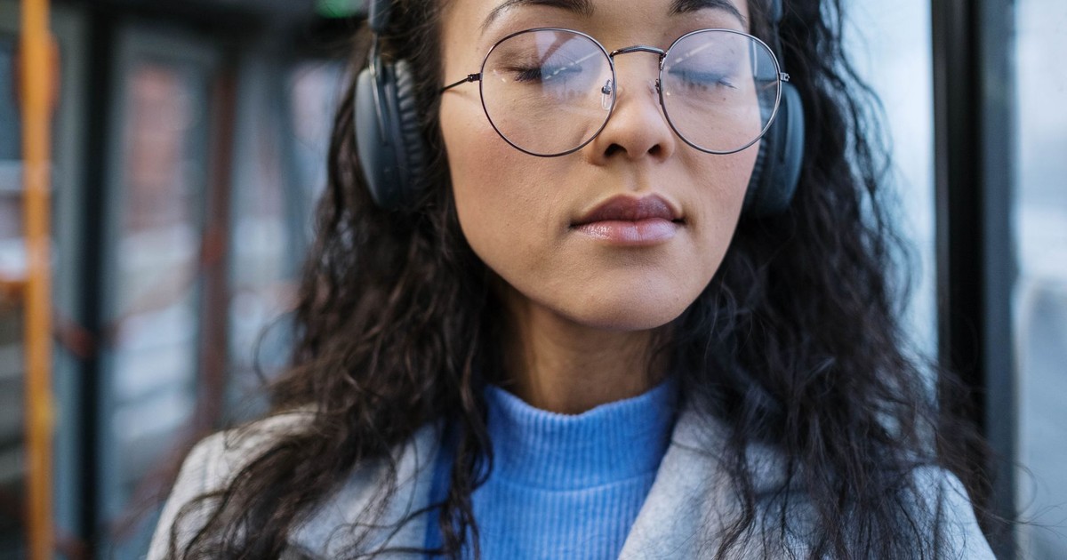 Portrait of a young woman with eyes closed, wearing headphones and glasses, enjoying music.