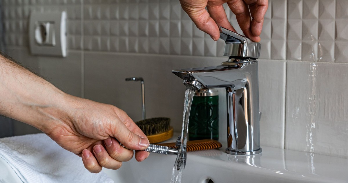 Close-up image of a man washing a shaver under a bathroom faucet, emphasizing cleanliness.