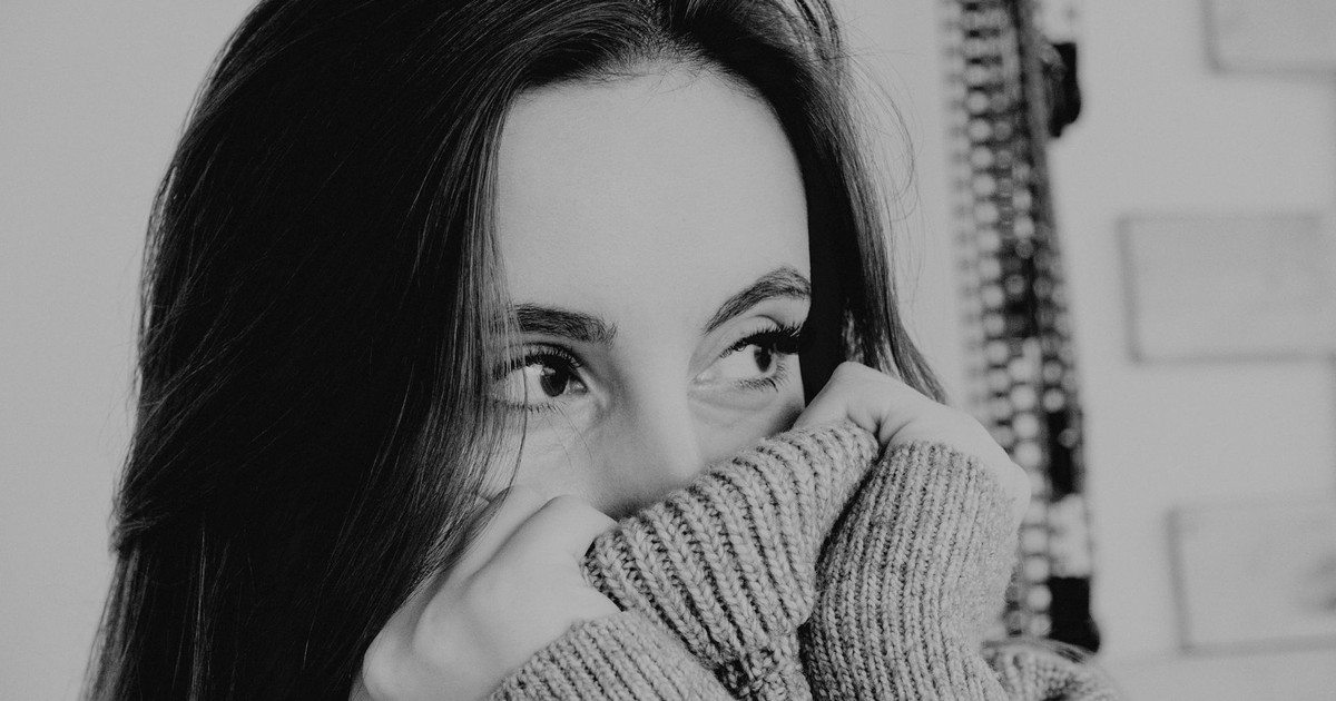 Black and white of female in warm sweater covering face with collar and looking away