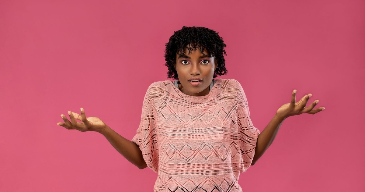 Young woman expressing confusion or uncertainty with a puzzled look on a pink background.