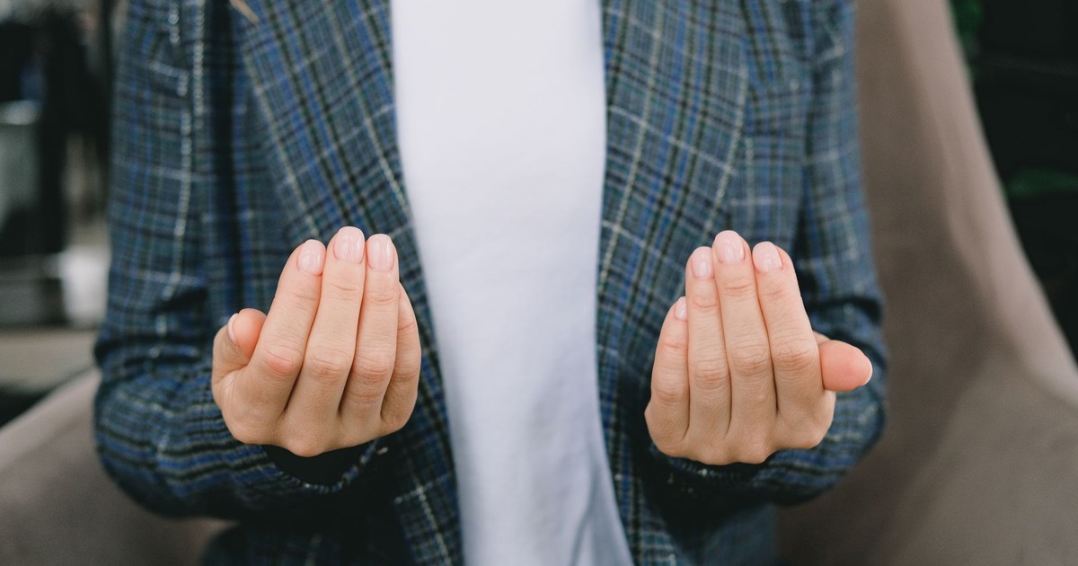 Close-up of a woman in a plaid blazer gesturing with open hands indoors.