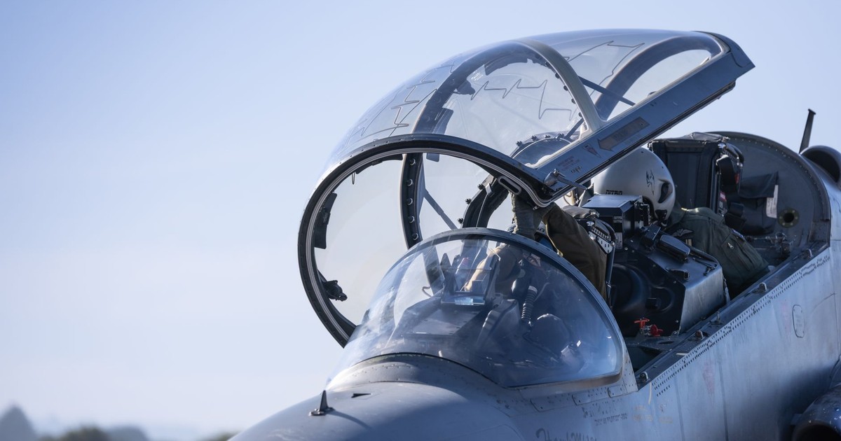Detailed view of a military jet cockpit with pilots preparing for flight against a clear sky.