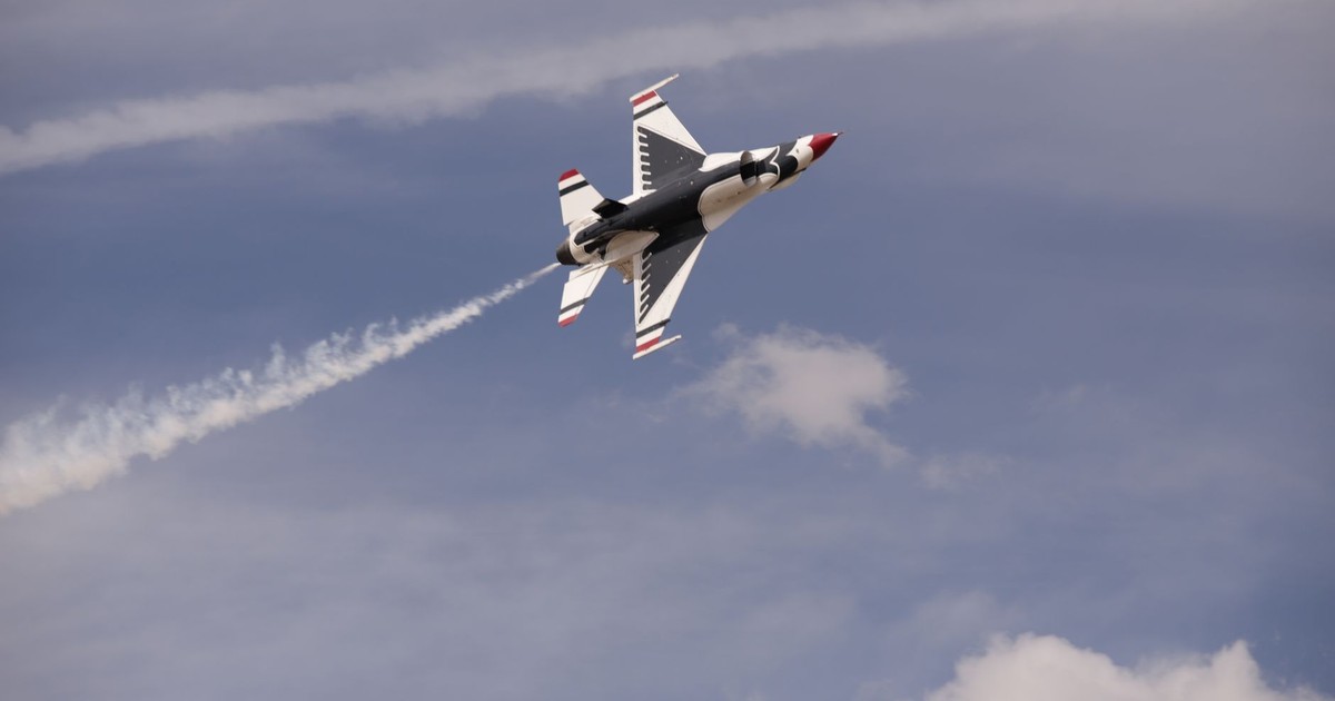 Jet fighter flying at high speed with vapor trails against a blue sky.