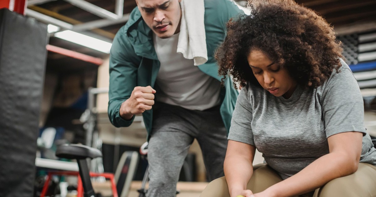 From below of strong personal coach explaining black woman how to exercise with dumbbells properly