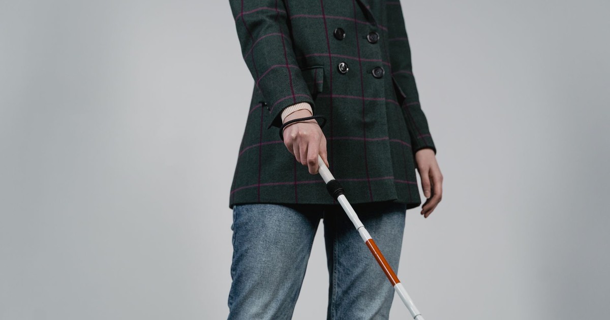 A person wearing casual clothes using a walking cane for assistance indoors.