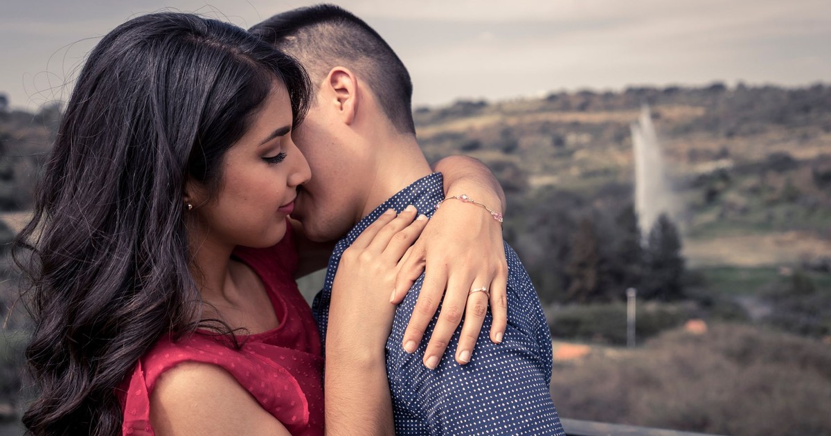 A loving couple embraces on an outdoor terrace overlooking scenic landscape.