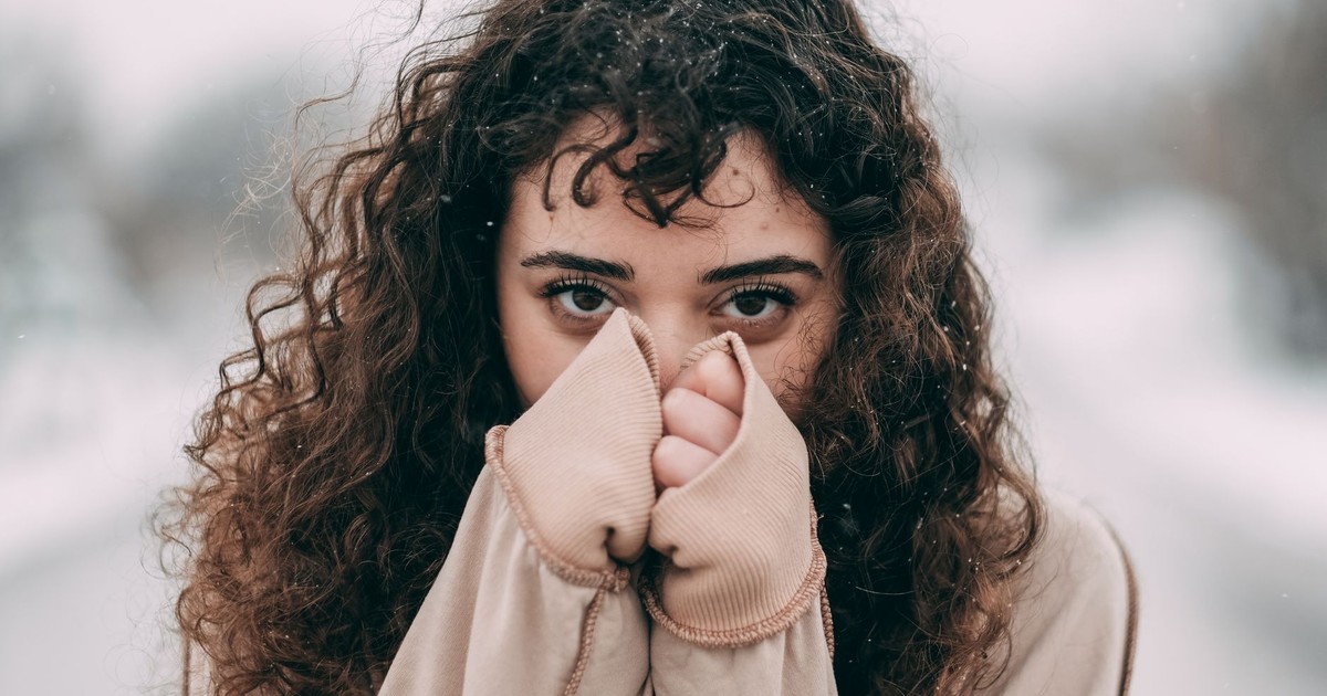 Close-up portrait of a young woman in a beige sweater outdoors during winter.