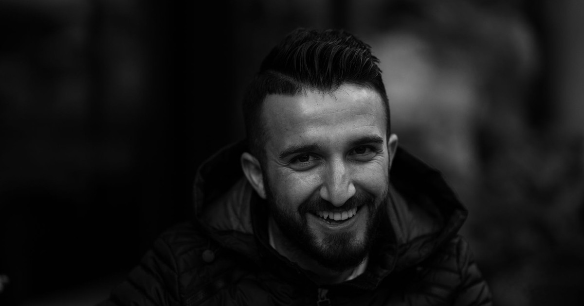 Captivating black and white portrait of a man with facial hair, smiling warmly against a blurred background.