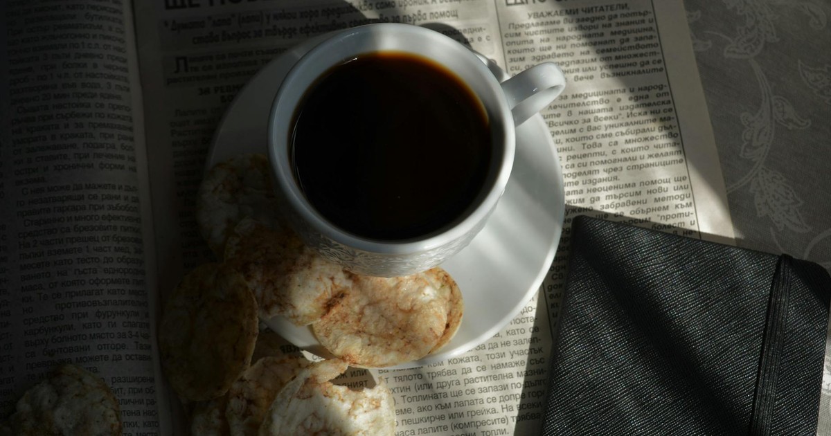 A cozy setup featuring a cup of black coffee, biscuits, and a newspaper, perfect for a relaxed morning.