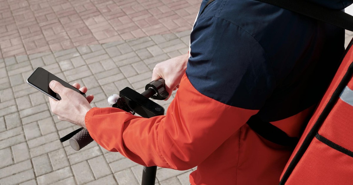 A delivery person riding an electric scooter using a smartphone for navigation outdoors.