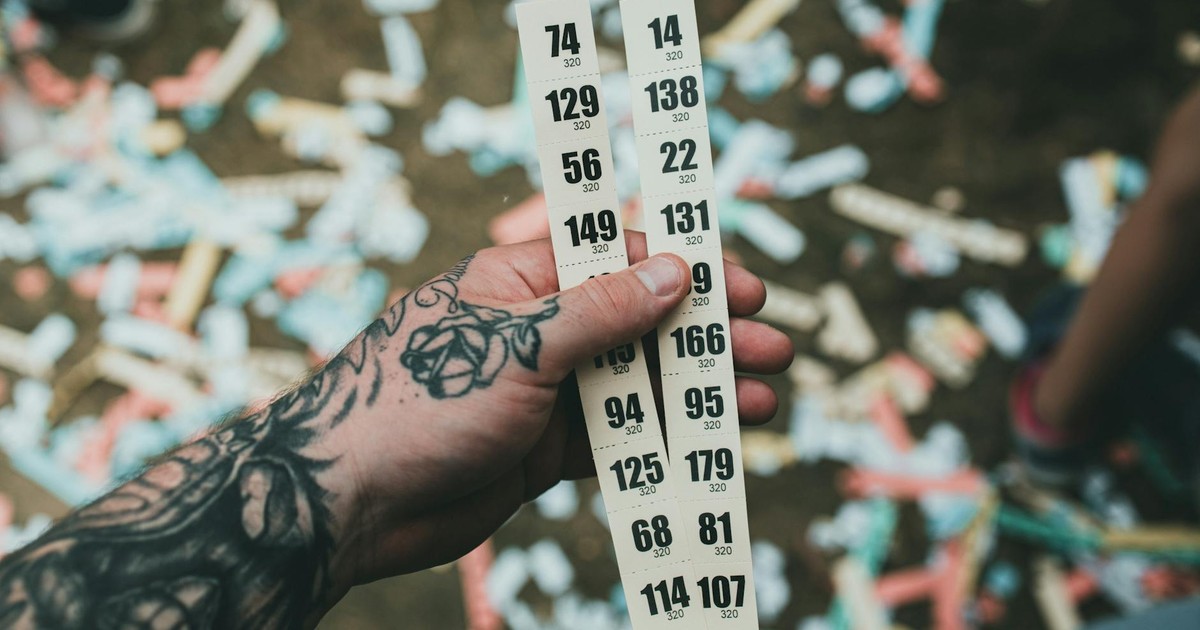 Close-up of a tattooed hand holding raffle tickets amidst confetti at a festival setting.