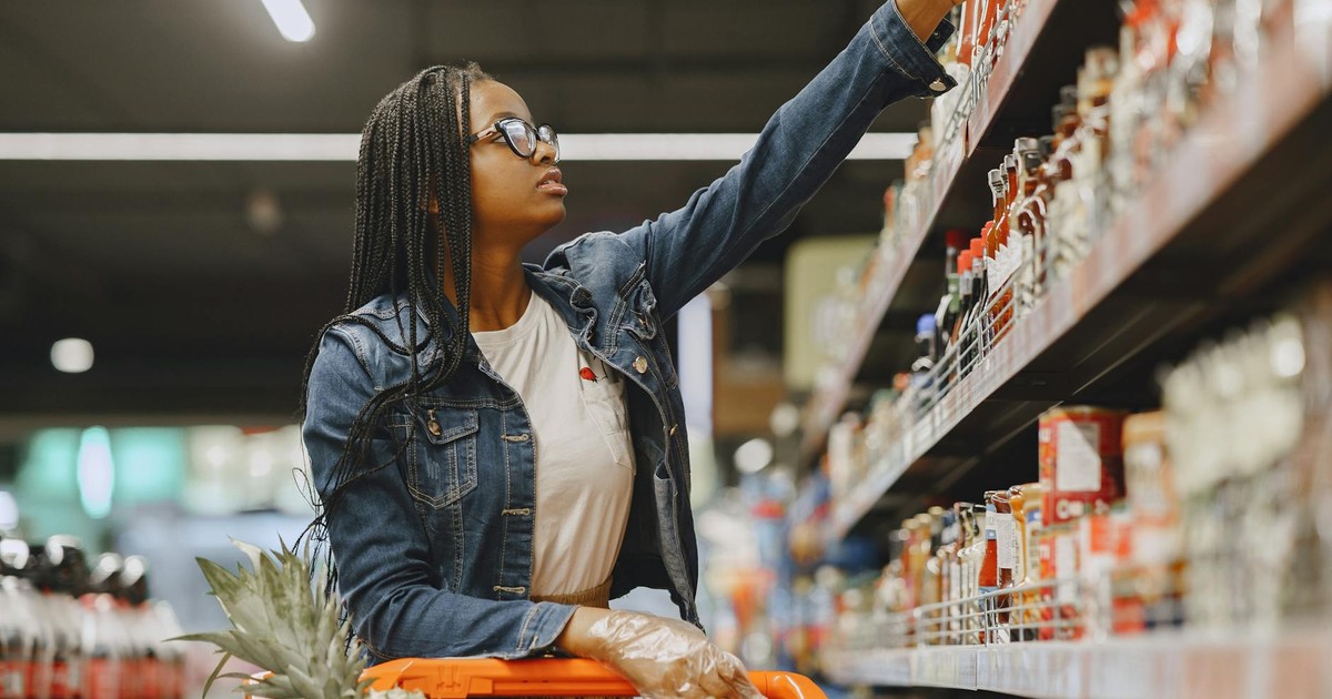 African American woman selecting items in a grocery store aisle with a shopping cart.