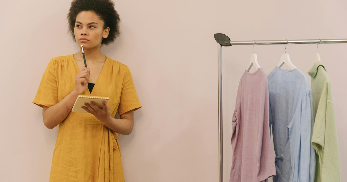 A woman in a yellow dress ponders creatively in a clothing studio with racks.