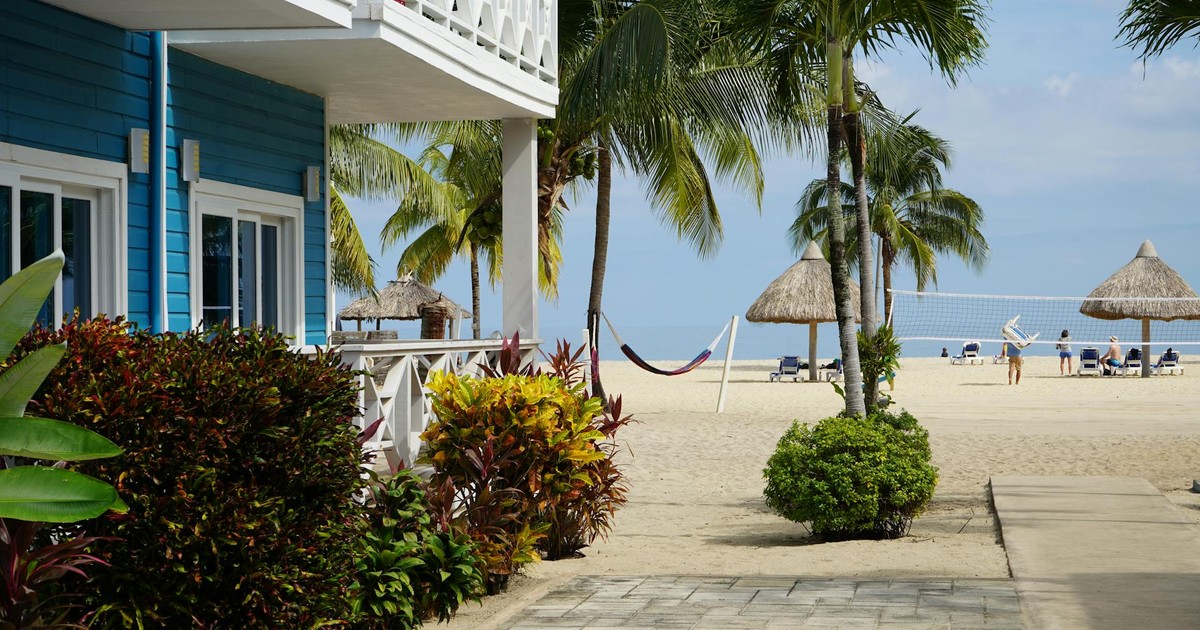 A vibrant beachfront villa in Placencia, Belize, surrounded by palm trees and a sandy beach with volleyball.
