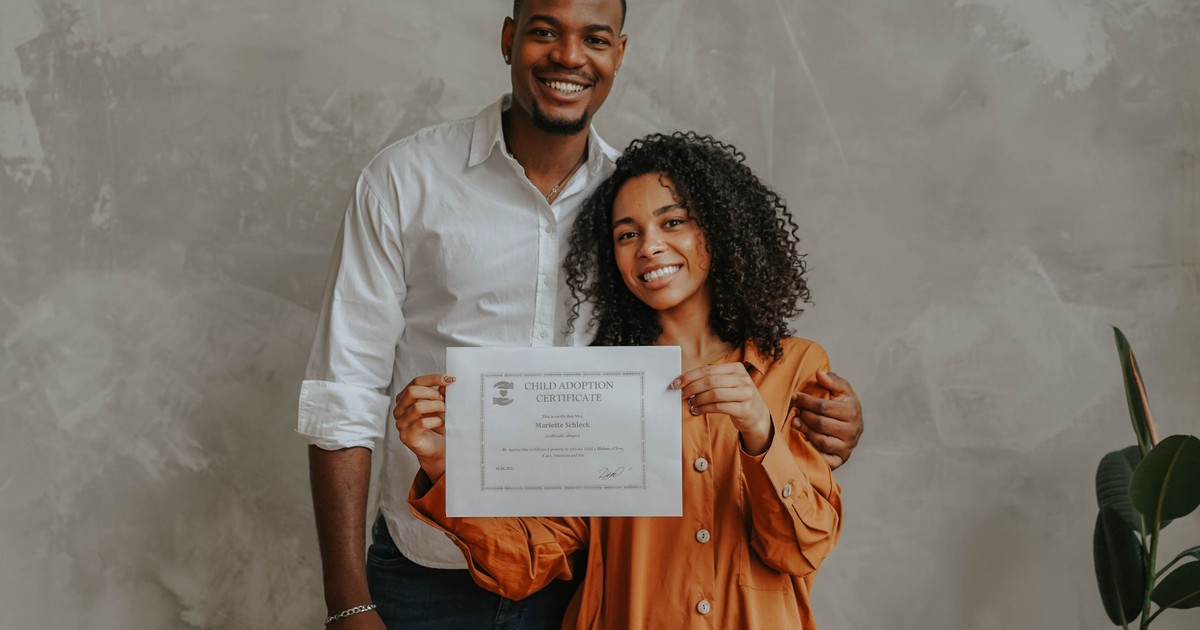 A joyful couple posing with their child adoption certificate indoors.