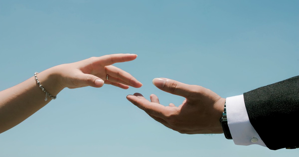 Close-up of two hands reaching towards each other under a clear blue sky, symbolizing connection.