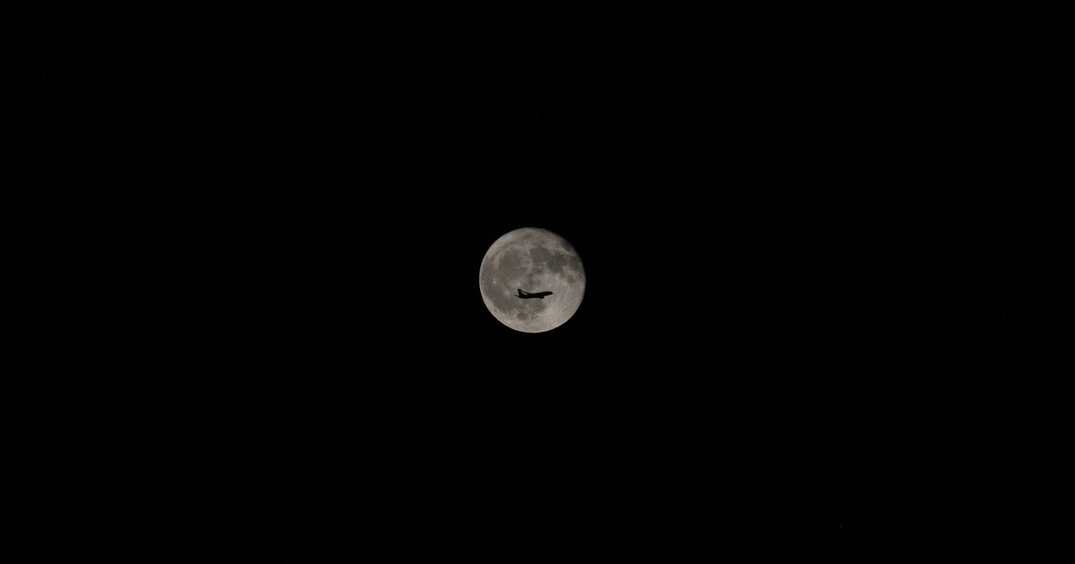 An airplane silhouette against a bright full moon in a clear night sky, showcasing travel and exploration.