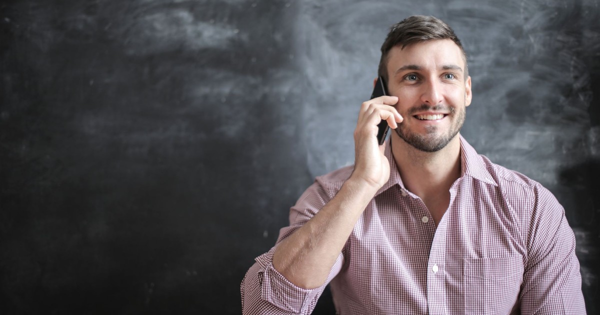 A cheerful man in a pink dress shirt talks on a smartphone, exuding positivity.