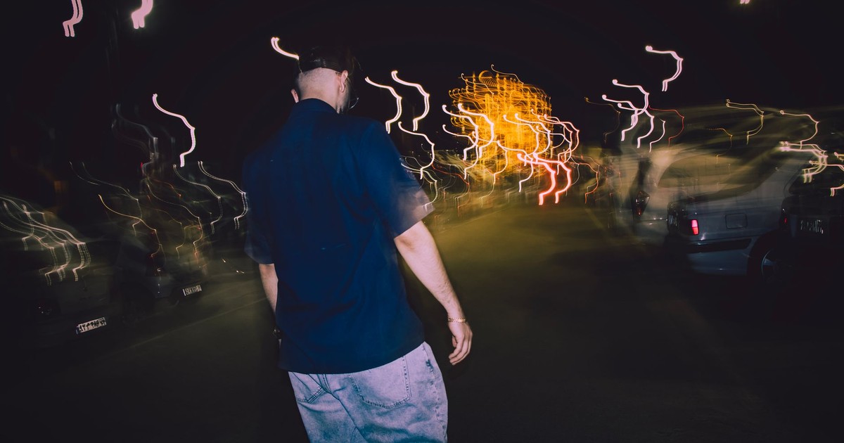 A man walks through a blurred street in Mashhad at night, creating a dynamic urban scene.