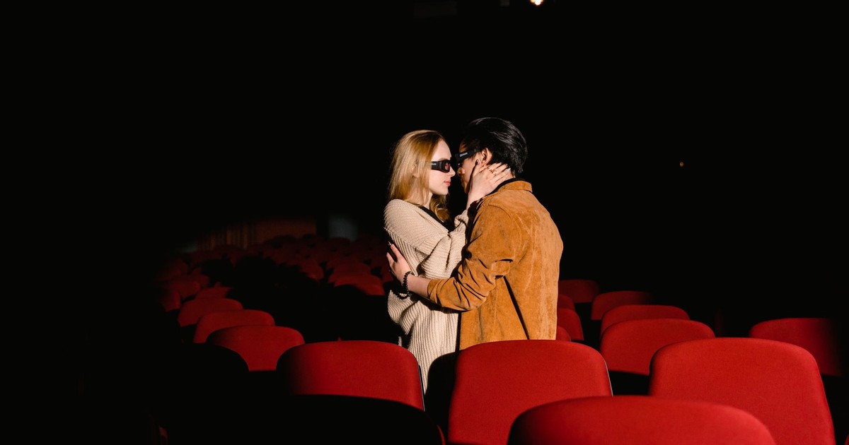 A romantic couple wearing 3D glasses embracing in an empty movie theater.