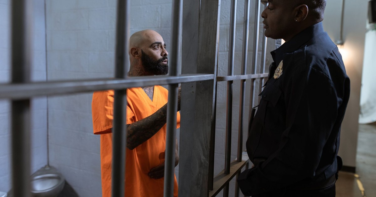 A guard converses with an inmate inside a prison cell, highlighting the justice system setting.