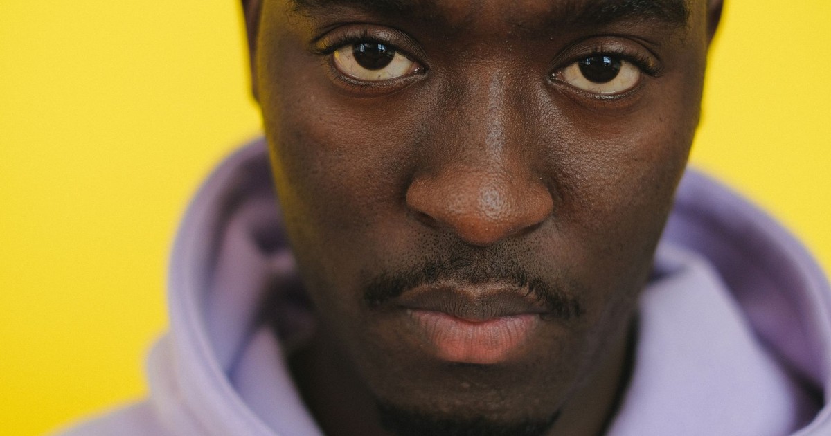 Crop unemotional African American male in hoodie gazing at camera seriously against yellow background