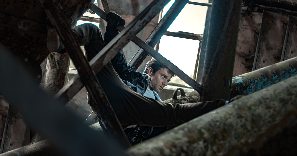A determined man maneuvering through a complex rusted metal framework in an industrial setting.