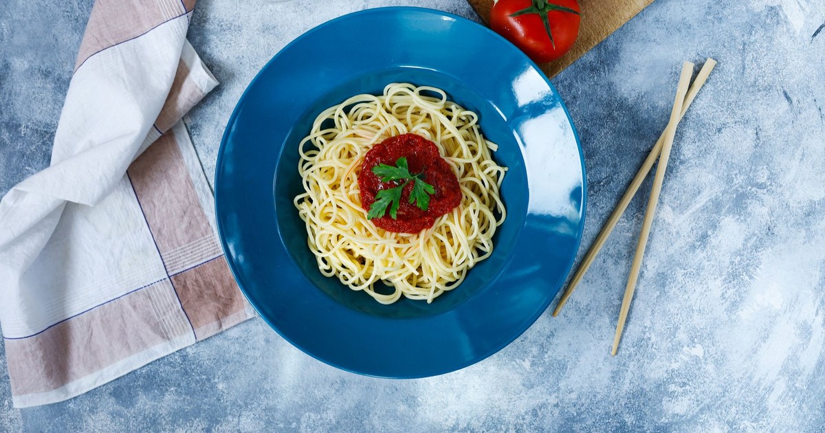 Top view of spaghetti with tomato sauce garnished with parsley, served on a blue plate.