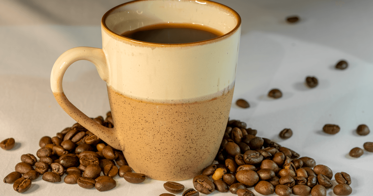 A warm cup of coffee surrounded by roasted beans on a white background.