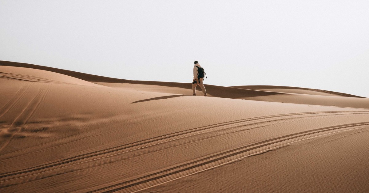 A lone man hiking across vast desert sand dunes with a backpack, showcasing adventure.