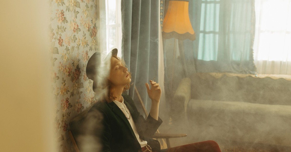 A man sits in a smoky, vintage-styled room, evoking nostalgia and relaxation.