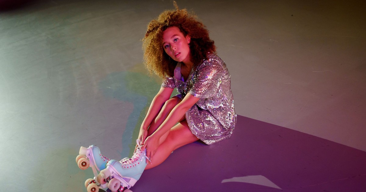 A woman in a sparkling sequin dress poses with roller skates on a floor, creating a fashionable and vibrant scene.