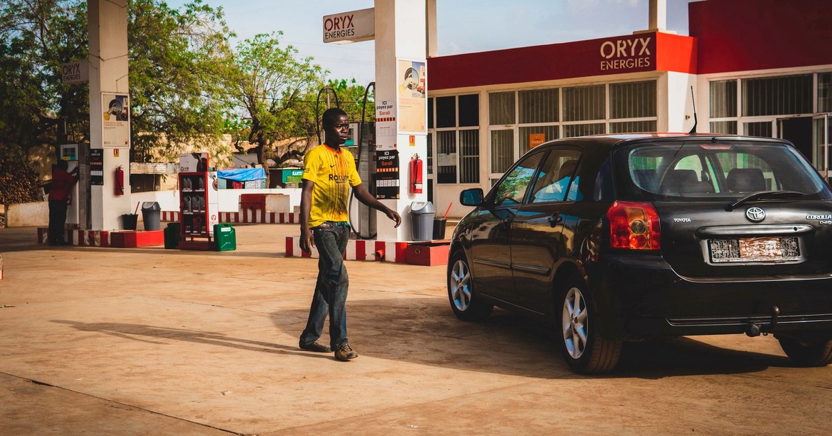 Man at a gas station fueling a black car under the bright daylight.