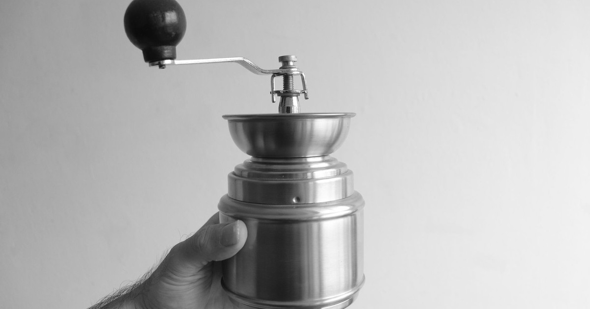 Classic black and white image of a hand holding a metal coffee grinder.