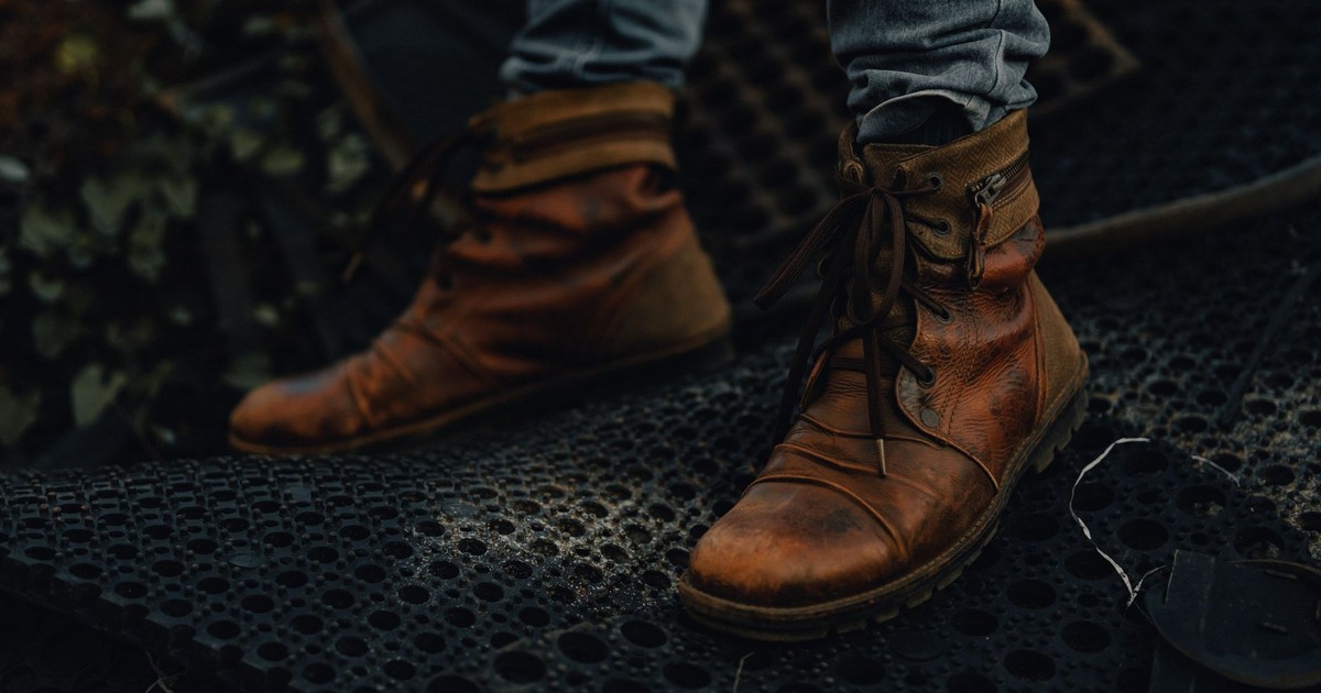 Close-up of brown leather boots on a textured dark surface. Urban and rugged feel.