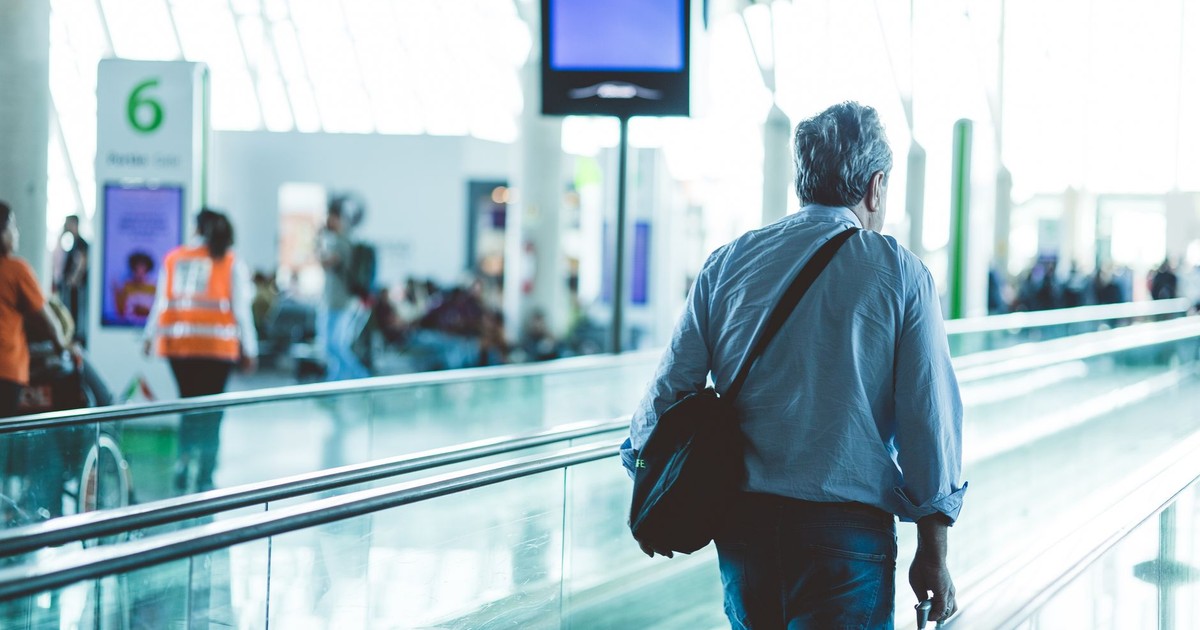 An adult male walking on an airport travelator, captured in a modern and well-lit terminal.