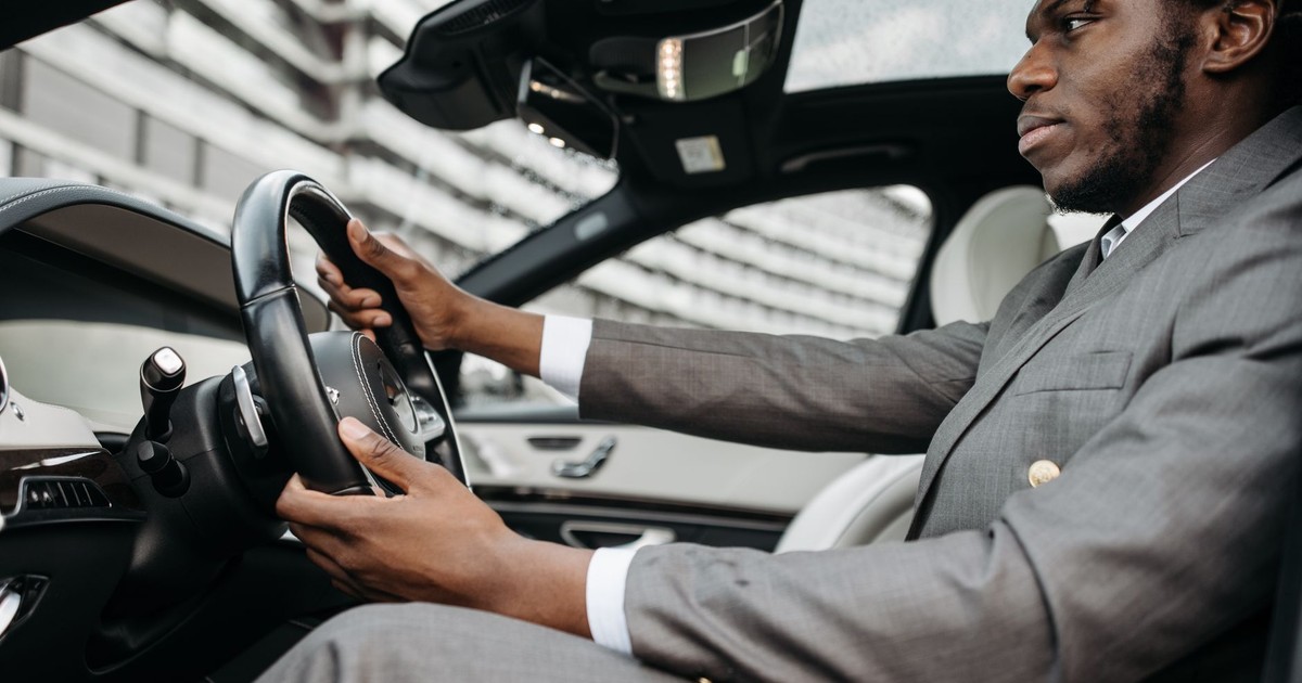 Man in a gray suit driving a luxury car, focused on the road.