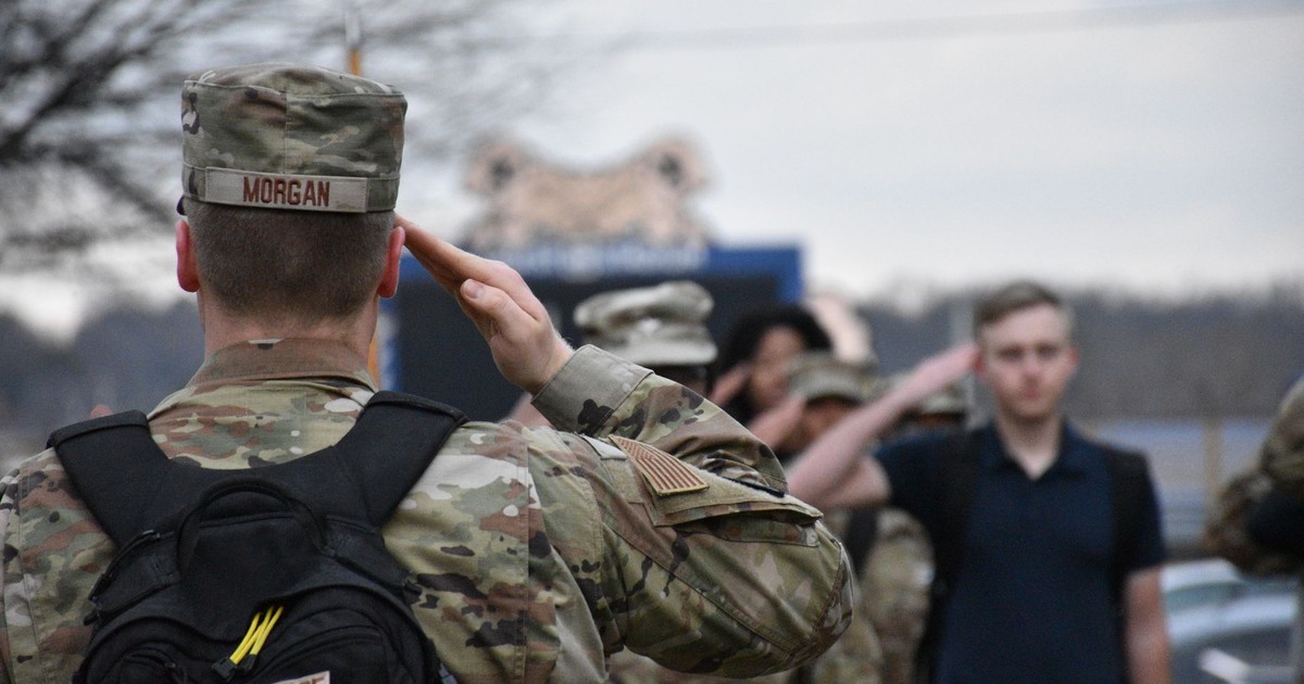 Group of soldiers in camouflage uniforms saluting, showing unity and respect outdoors.