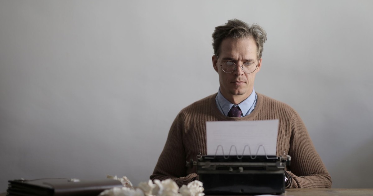 A thoughtful male writer typing on a vintage typewriter, surrounded by crumpled papers.