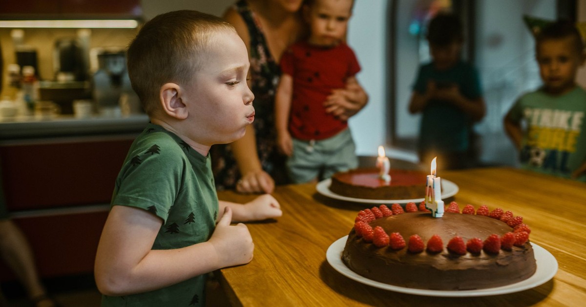 Young boy celebrating birthday by blowing candles on chocolate cake with raspberries.