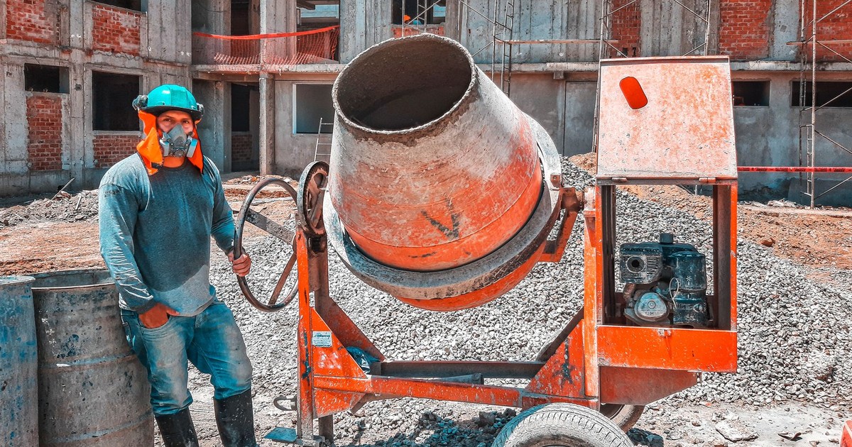 A construction worker operating a concrete mixer at an active building site, emphasizing safety gear.