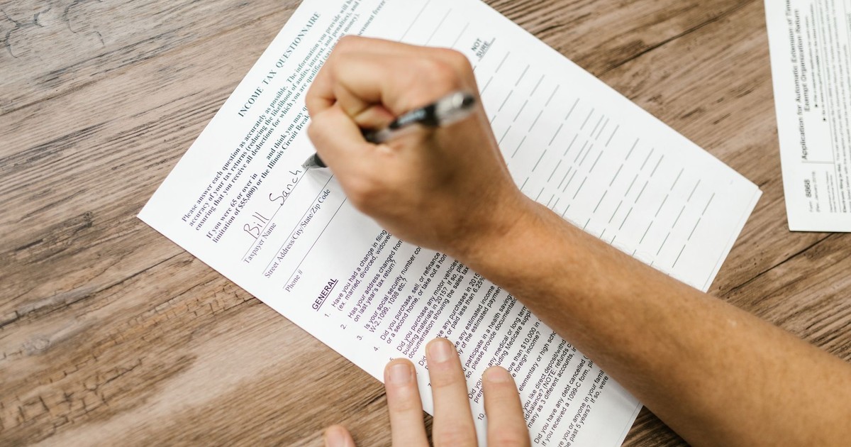 Person filling out a tax questionnaire with a pen, showing close-up on wooden table.