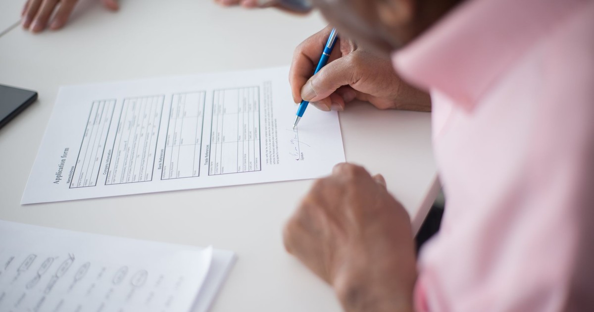 Elderly man signing important business document at desk in office setting.